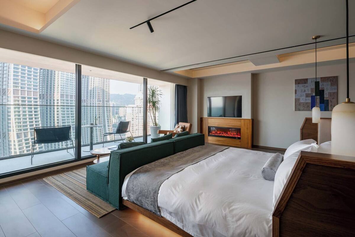 Habitación de hotel moderna con una cama grande, televisor, chimenea y balcón con vistas a la ciudad.