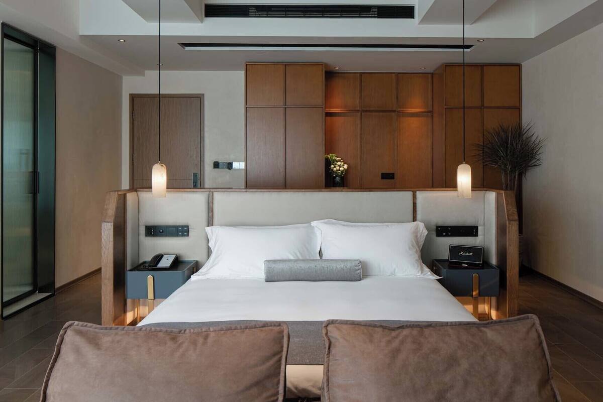 Un dormitorio moderno con una cama grande, mesitas de noche, un pequeño escritorio y aire acondicionado de pared, además de un ventanal amplio.