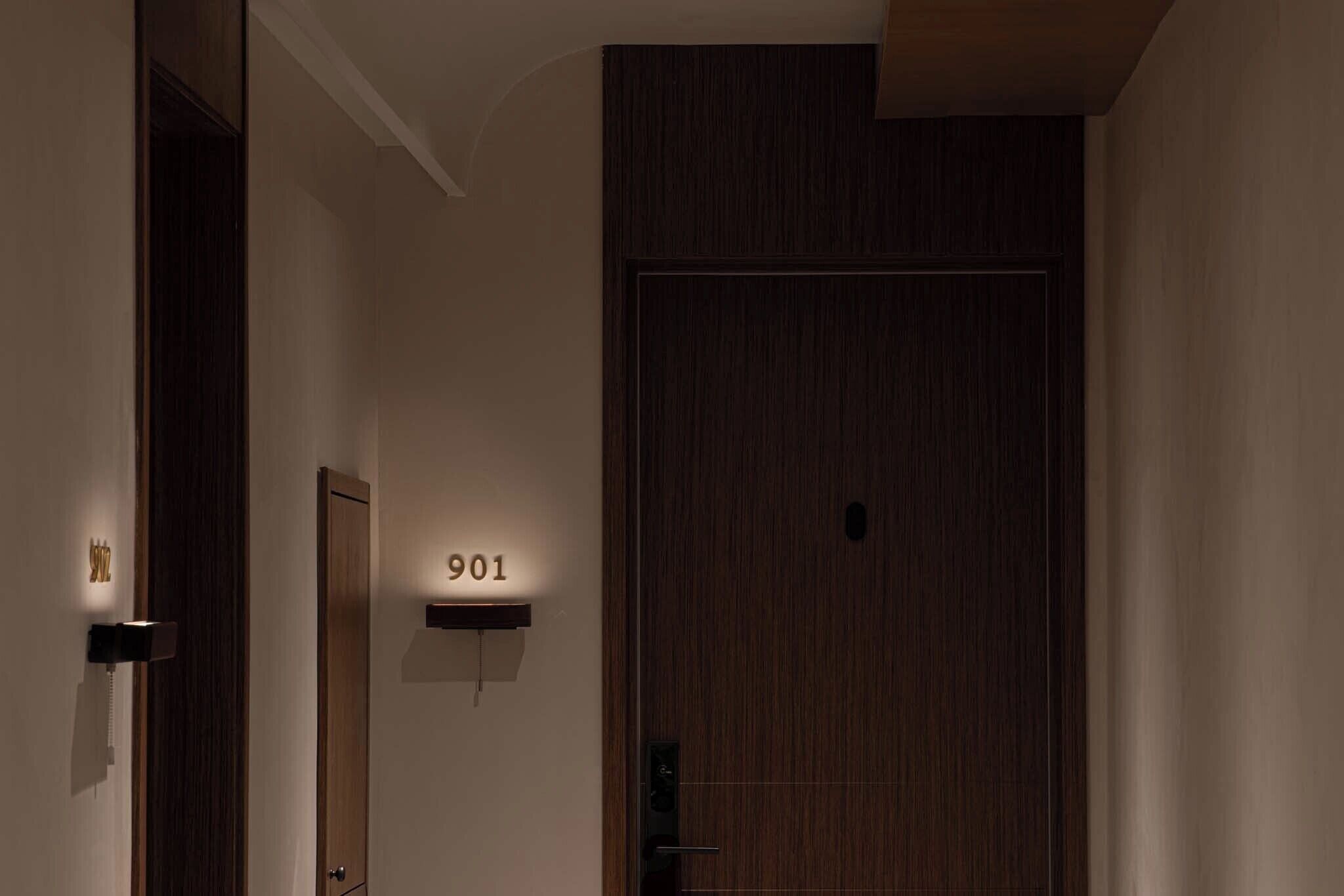 Un pasillo con una puerta de madera con la etiqueta '901' y un teléfono en la pared.