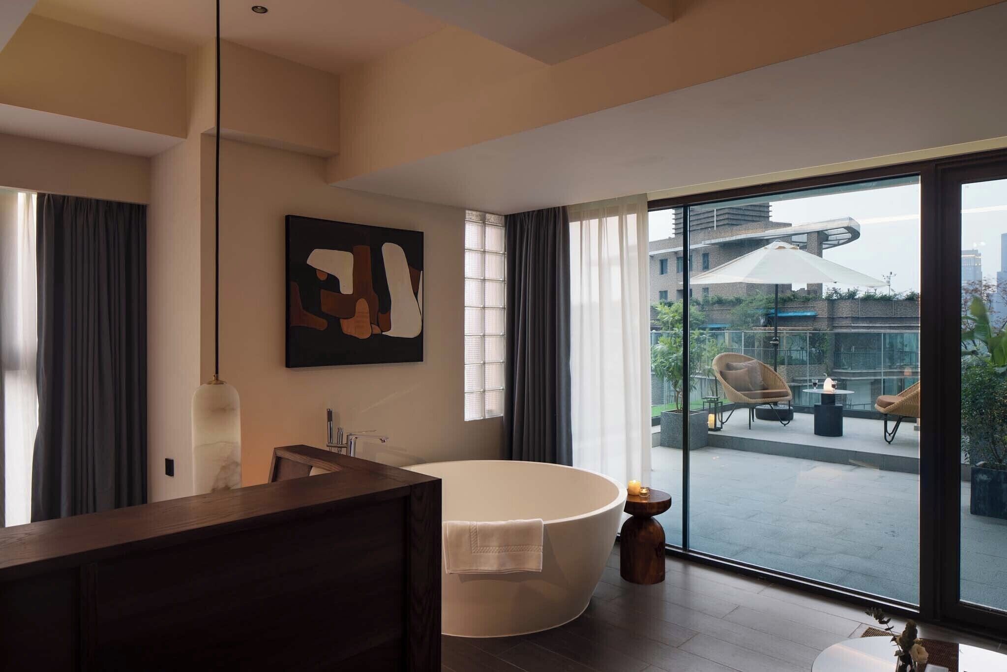 A modern bathroom with a freestanding bathtub, a large mirror, and a contemporary artwork on the wall.