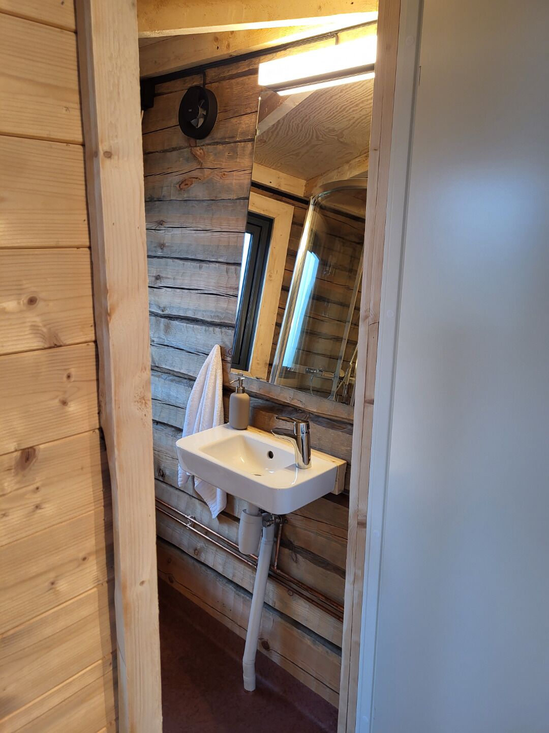 A wooden cabin bathroom with a white sink, a mirror, and a towel hanging on the wall.