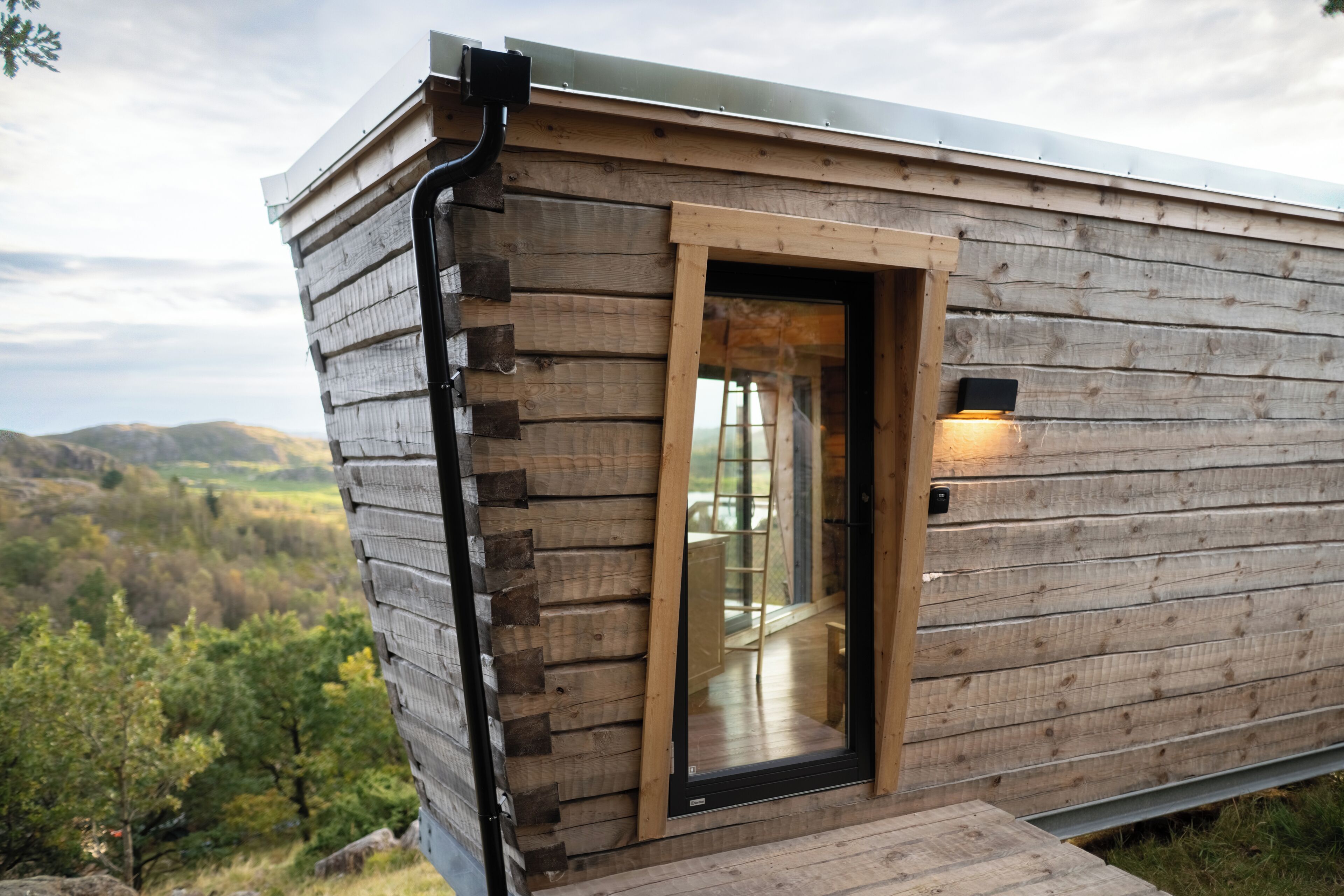 A wooden cabin with a glass door, a small deck, and a view of the surrounding landscape.