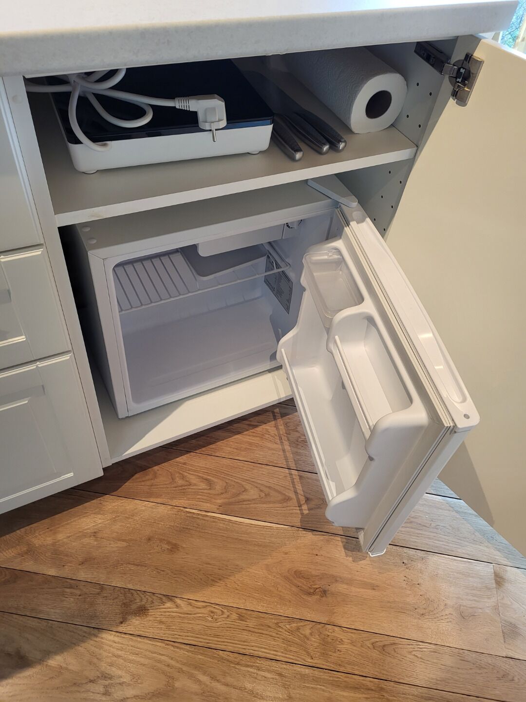 Una cocina con microondas integrado, un refrigerador blanco y piso de madera.