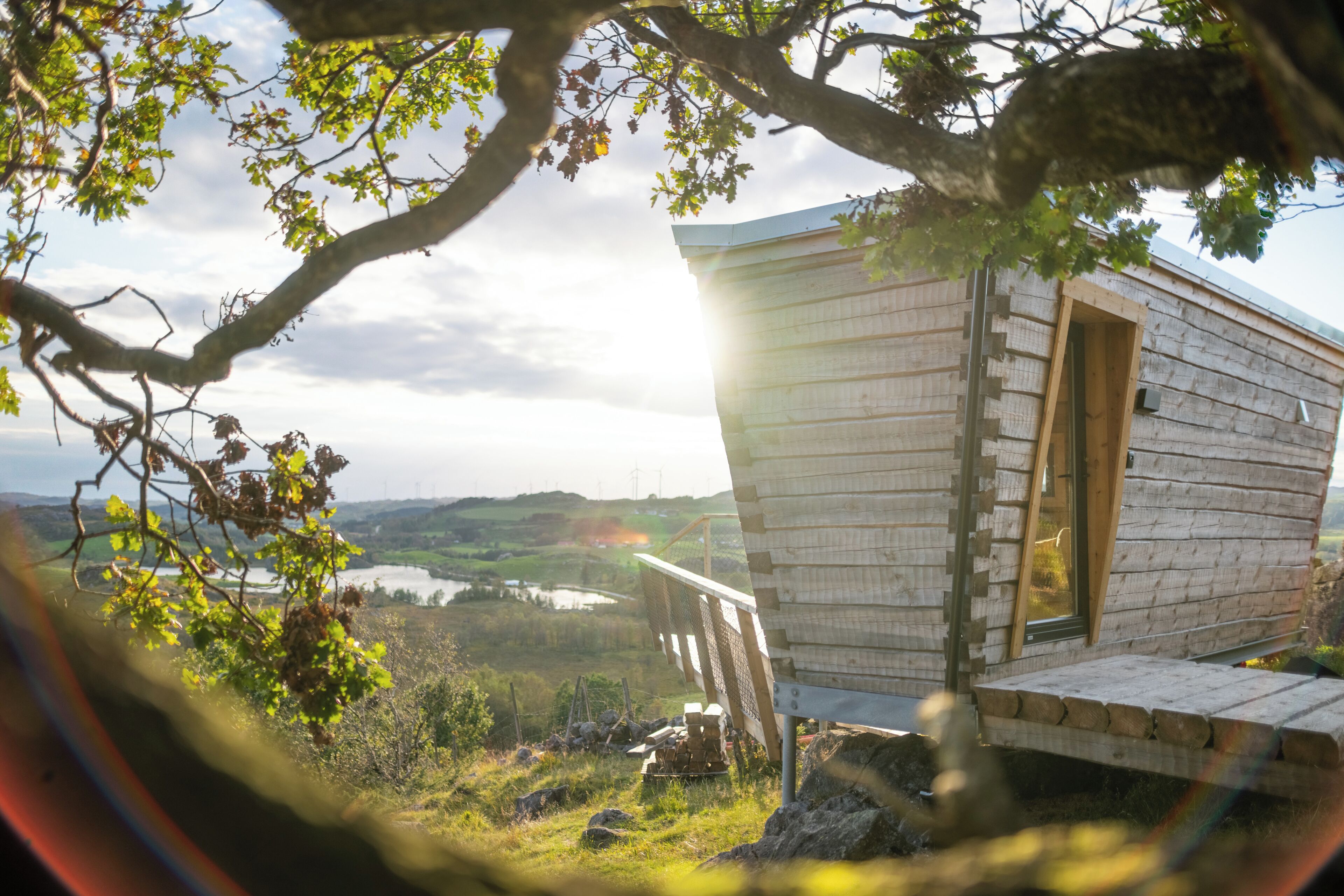 A wooden cabin with a door, a small porch, and a view of a lake and hills in the background.