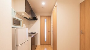 A narrow hallway with a wooden door at the end, a microwave, and a refrigerator. - b&Imazato (Osaka)