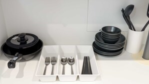 A kitchen counter with a black frying pan, a white tray with cutlery, and stacked black bowls. - b&Imazato (Osaka)