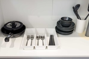 Un comptoir de cuisine avec une poêle noire, un plateau blanc contenant des couverts et des bols noirs empilés.