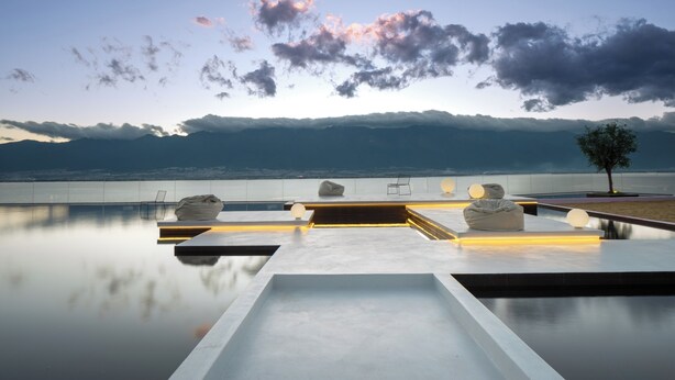 Ein moderner Infinity-Pool mit freiem Blick auf Berge und eine Stadtlandschaft im Hintergrund.
