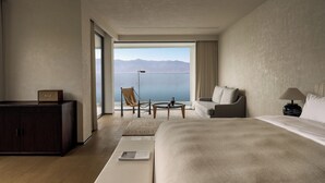 Ein modernes Hotelzimmer mit einem großen Bett, einer Sitzecke mit Meerblick und einem Schreibtisch mit Lampe.