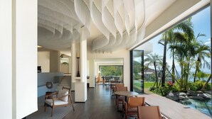 Ein modernes Interieur mit Essbereich, Treppe und großem Fenster mit Blick auf einen Pool und eine tropische Landschaft.