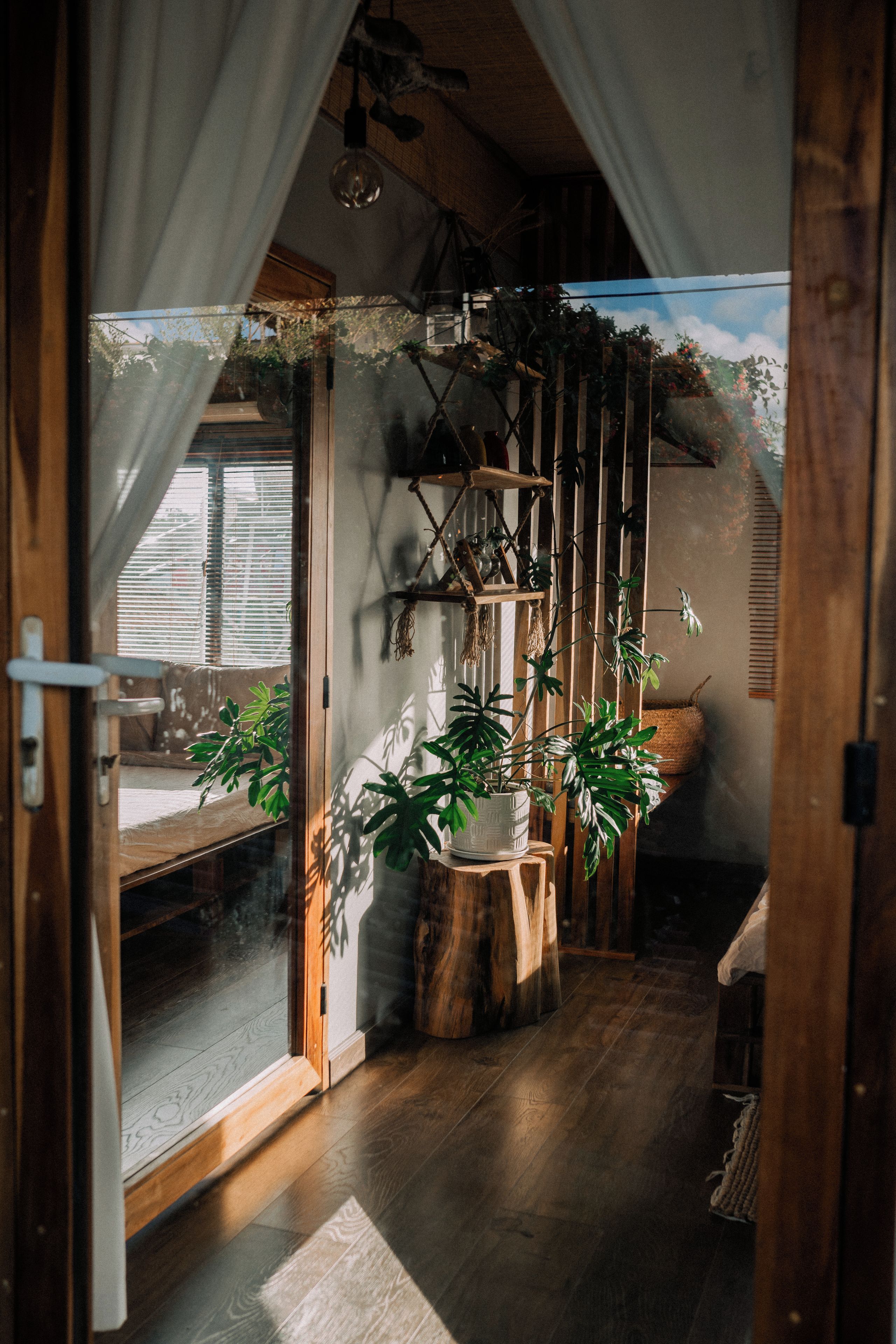 A room with wooden flooring, a large window with blinds, and a wooden staircase leading to an upper level.