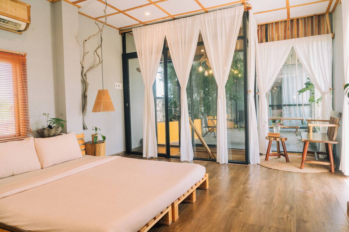 Une chambre avec un grand lit, un plancher en bois et une vue sur l’extérieur grâce à une porte vitrée.