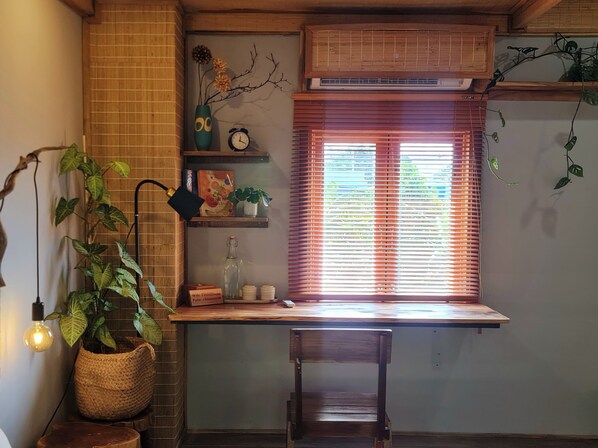 A cozy room with a wooden desk, a hanging lamp, a potted plant, a wall clock, and a window with blinds. - TINH Retreat Phu Quoc (Phu Quoc)