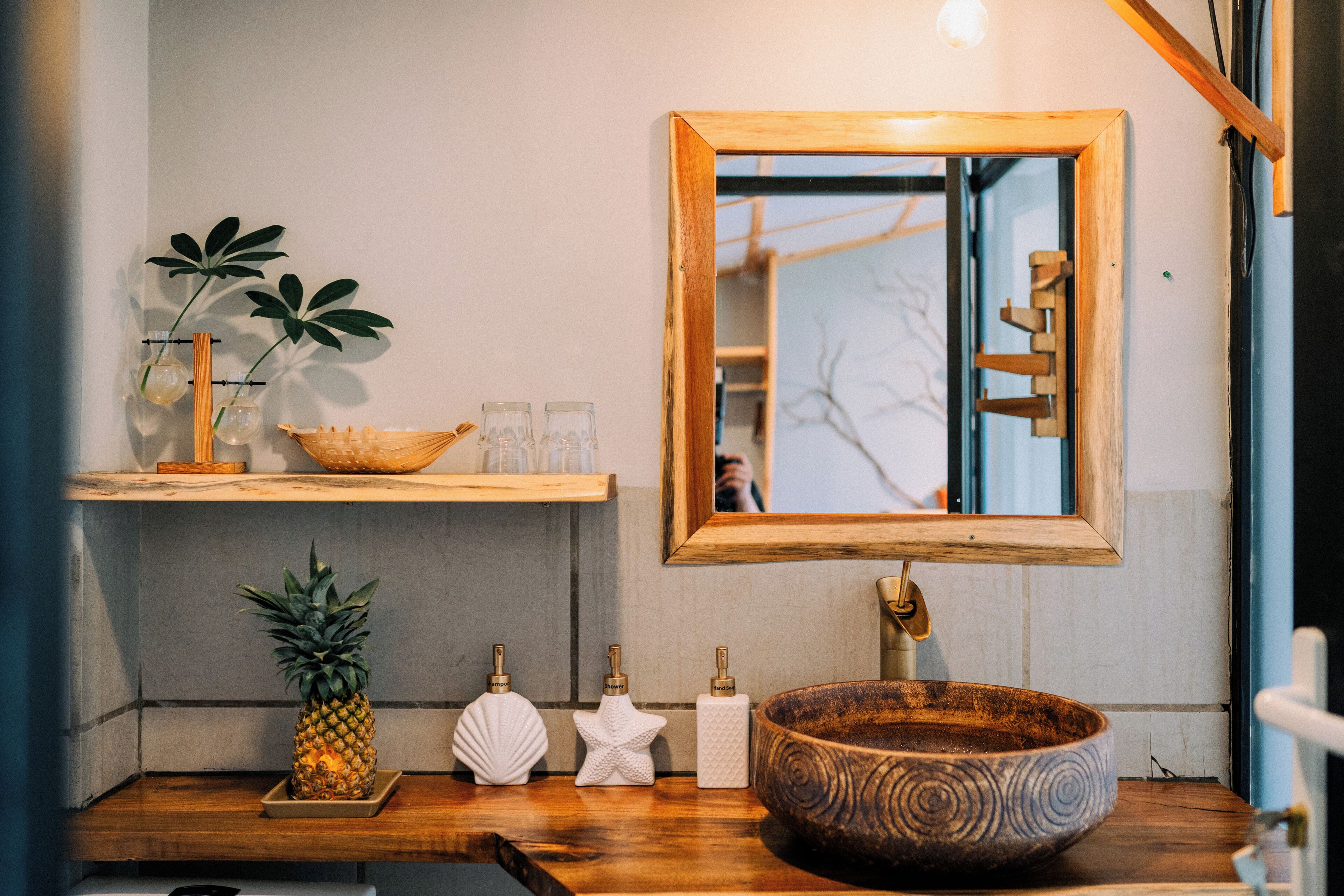 A bathroom with a wooden vanity, a large bowl sink, a mirror, and a shelf with a plant and toiletries.