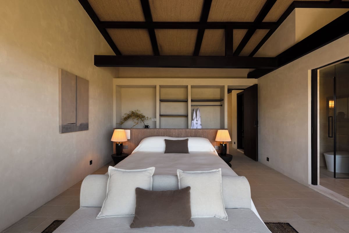 Una habitación de hotel moderna con una cama grande, techo de madera y puerta de cristal que da al baño.