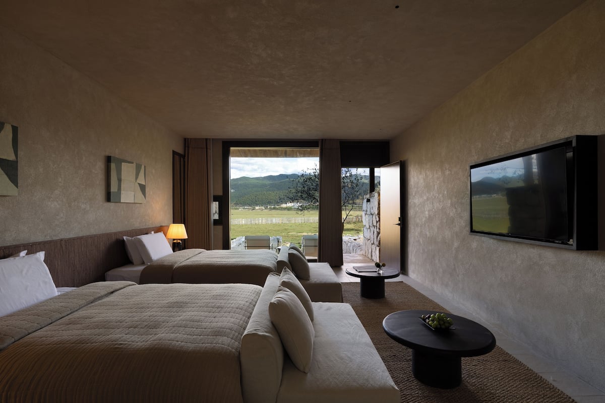 Habitación de hotel con dos camas, un sofá, televisión y balcón con vistas a las montañas.