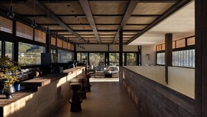 A modern interior with a long counter, wooden stools, and large windows offering a view of the outdoors. - Shangri-La Bandu Xingye Muge Manor Hotel (Deqin)