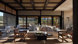 A spacious living area with a sofa, chairs, and a coffee table. Large windows offer a view of the outdoors. - Shangri-La Bandu Xingye Muge Manor Hotel (Deqin)