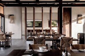 Une vaste salle à manger agrémentée de poutres en bois apparentes, de chaises en osier et de tables dressées pour le repas.