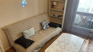 A beige sofa with a quilted backrest and two pillows, a marble-patterned coffee table, and a wooden herringbone floor. - Le Pégase 2 (Courseulles-sur-Mer)