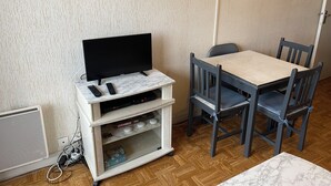 A room with a television on a stand, a Scrabble game, and a table with chairs. - Le Pégase 2 (Courseulles-sur-Mer)
