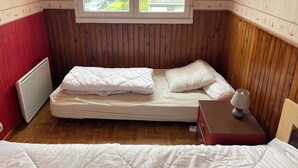 A bedroom with a wooden paneled wall, a window with a view of the outside, a bed with white bedding, a bedside table with a lamp, and a red suitcase. - Le Pégase 2 (Courseulles-sur-Mer)