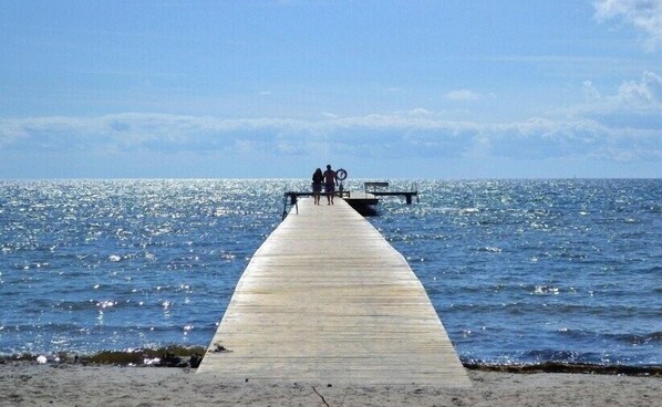 A wooden pier extending into a body of water with two people walking towards a dock.