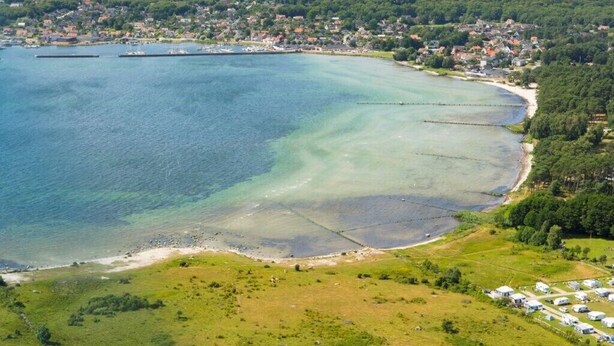 An aerial view of a coastal town with a marina, clear waters, and a mix of residential and commercial buildings. - hälleviks camping  (Sölvesborg)