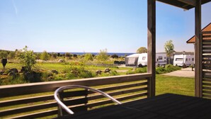 A covered outdoor seating area with a view of a grassy field and a body of water. - hälleviks camping  (Sölvesborg)