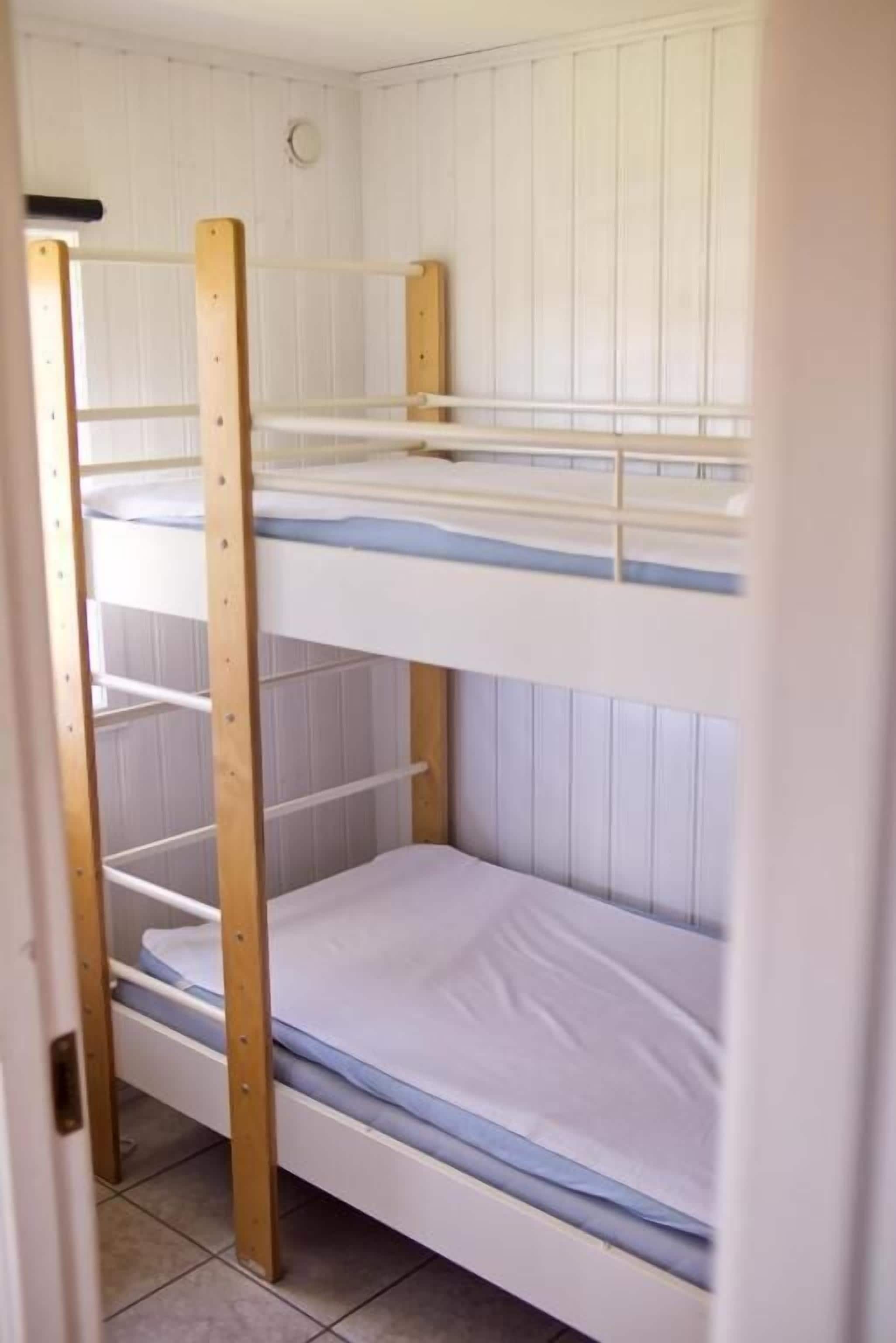 Cama litera con tres niveles, ropa de cama blanca y estructura de madera.