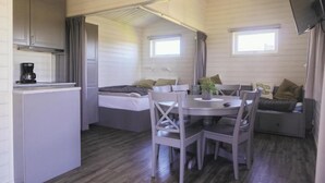 A compact room with a kitchenette, a dining area with a table and chairs, a bed, and a TV mounted on the wall. - hälleviks camping  (Sölvesborg)