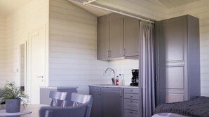 A compact room with a bed, a small kitchenette with cabinets, a sink, and a dining area with chairs. - hälleviks camping  (Sölvesborg)