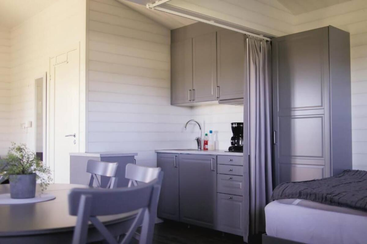 A compact room with a bed, a small kitchenette with cabinets, a sink, and a dining area with chairs.
