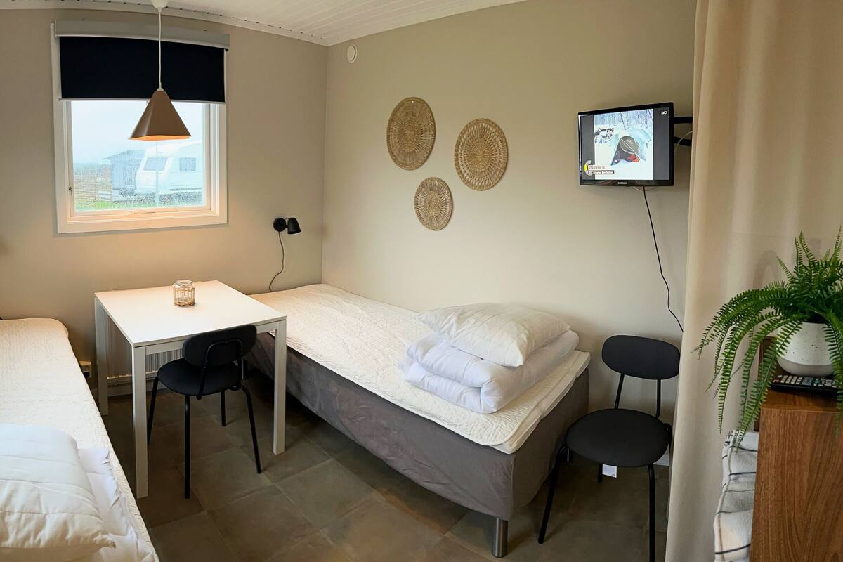 A small, well-lit room with two single beds, a desk, and a TV.