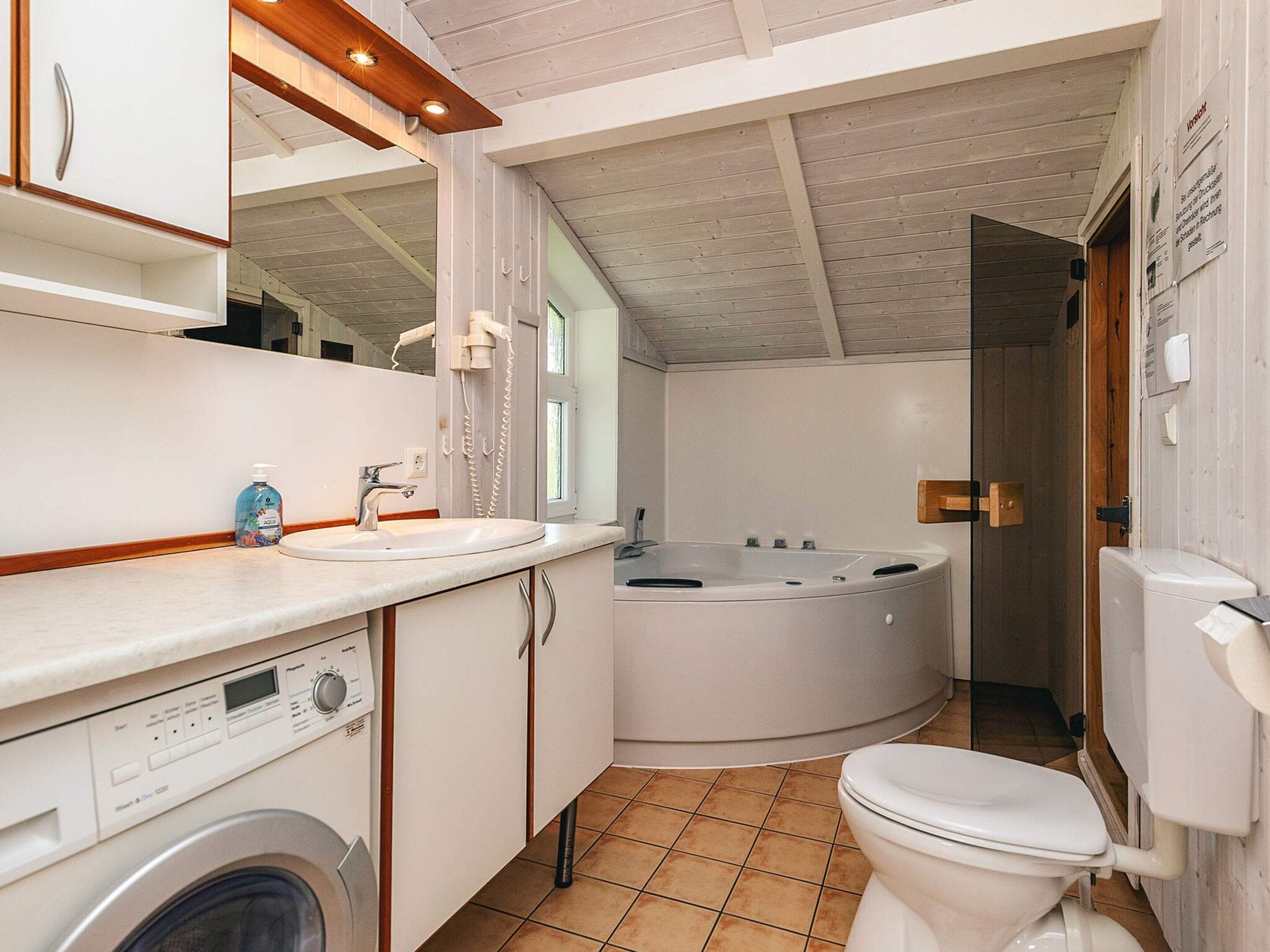 A modern bathroom with a built-in washing machine, a large bathtub, and a toilet.