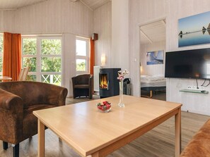 A room with a wooden table, two armchairs, a fireplace, a television, and a window with curtains.