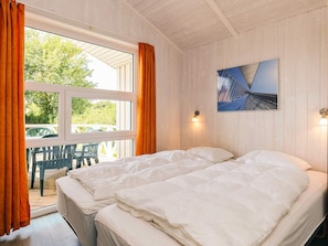 A double bed with white bedding in a room with wooden walls and a window with curtains. - 4 Star Holiday Home in Friedrichkoog (Friedrichskoog)