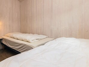 A bedroom with two beds, wooden panel walls, and a nightstand with a lamp.