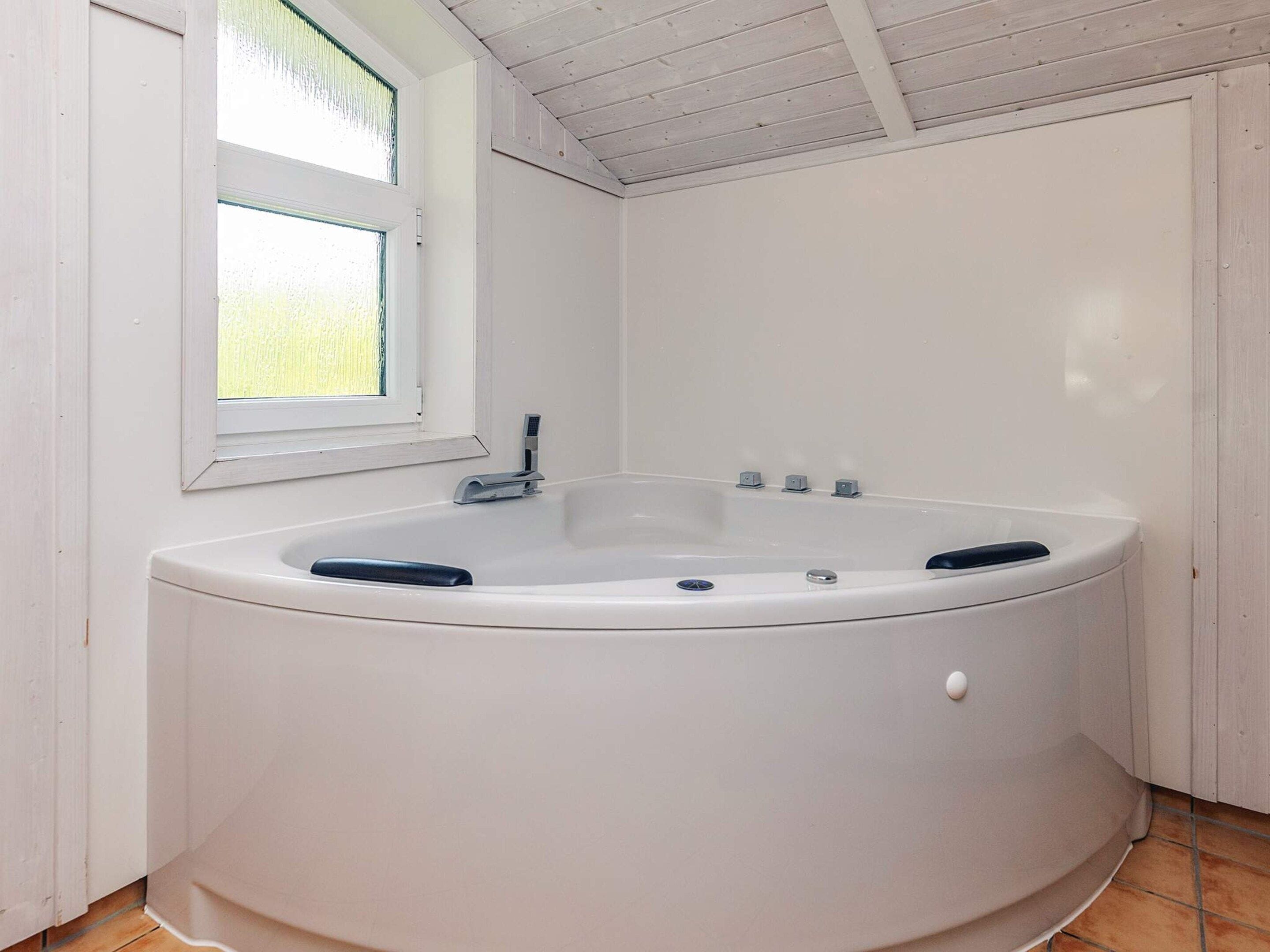 A white bathtub in a room with white walls and a window.