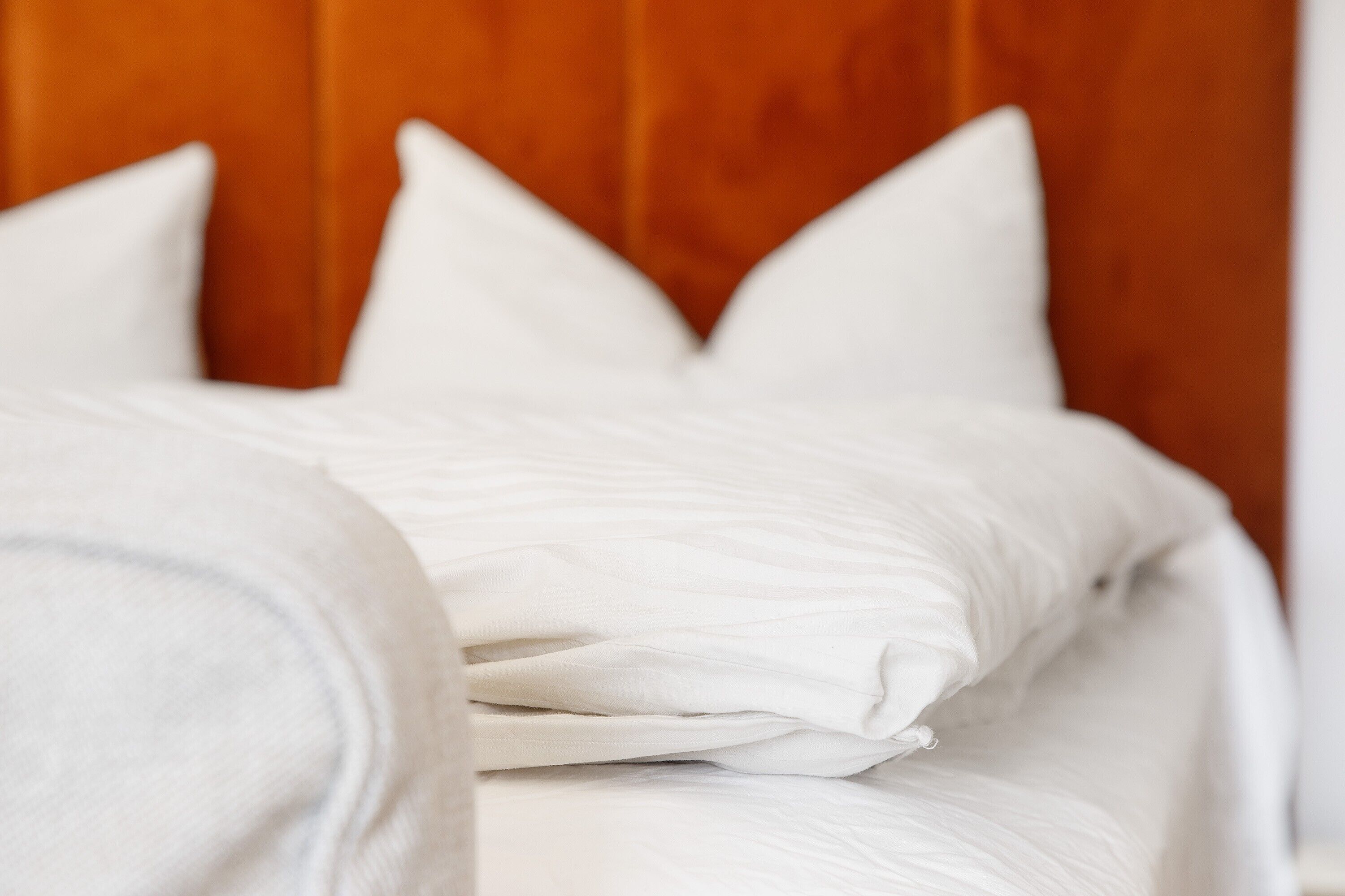 A bed with white bedding and pillows, a wooden headboard, and a white wall.