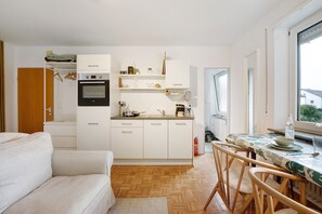 A compact kitchen with white cabinetry, a built-in oven, and a dining area with a table and chairs.