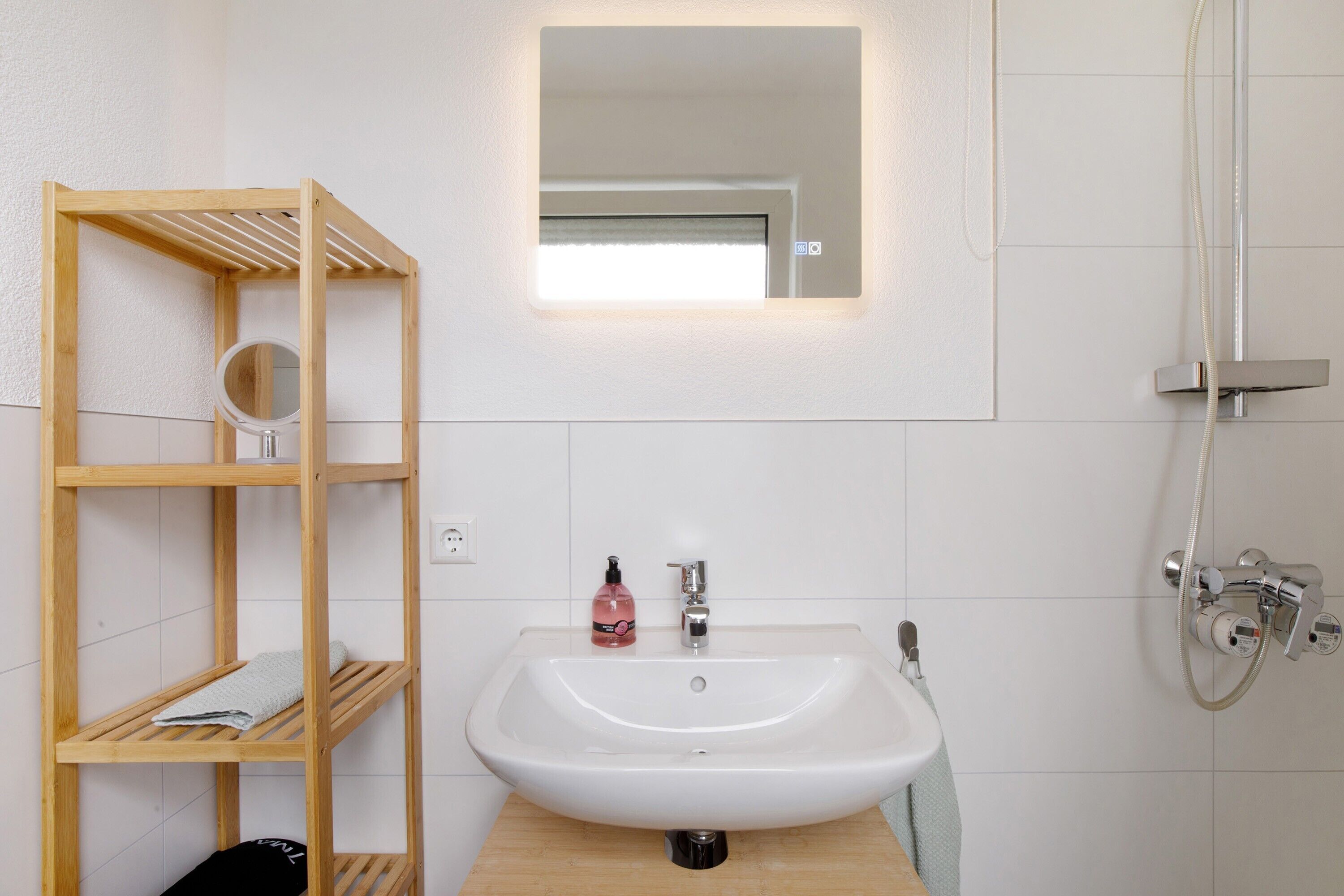 Une salle de bain avec une étagère en bois, un lavabo, un miroir et une douche.