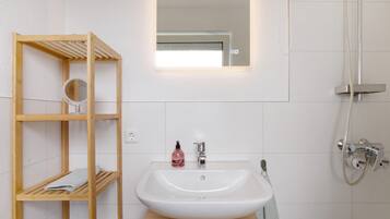 Une salle de bain avec une étagère en bois, un lavabo, un miroir et une douche.