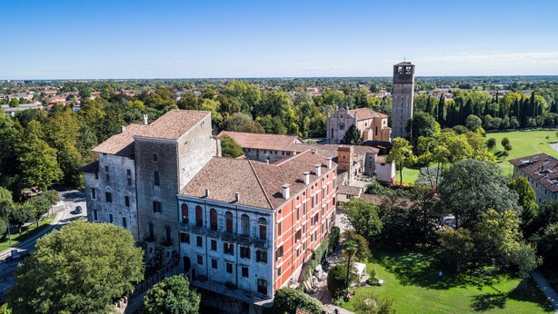 Un complejo arquitectónico histórico con varias edificaciones, incluyendo una torre destacada, rodeado de abundante vegetación y un cielo despejado.