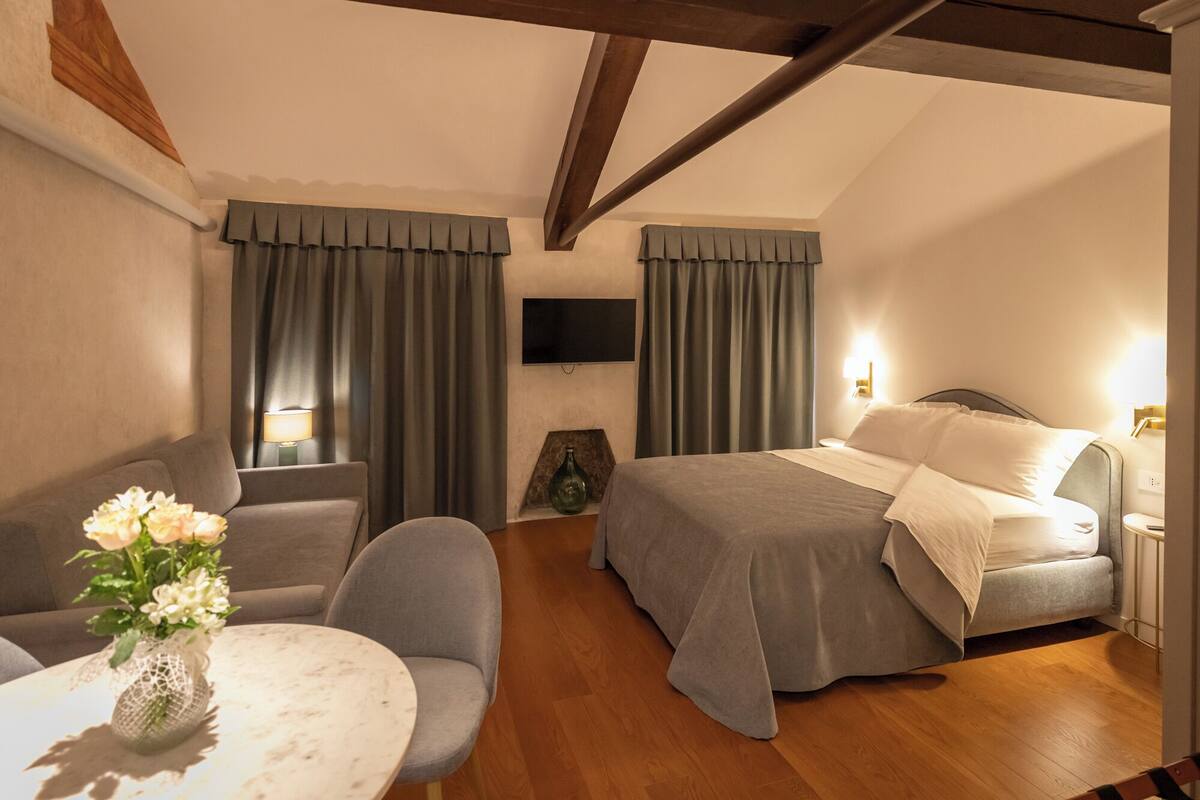A hotel room with a bed, a seating area with a table and chairs, a TV mounted on the wall, and curtains.
