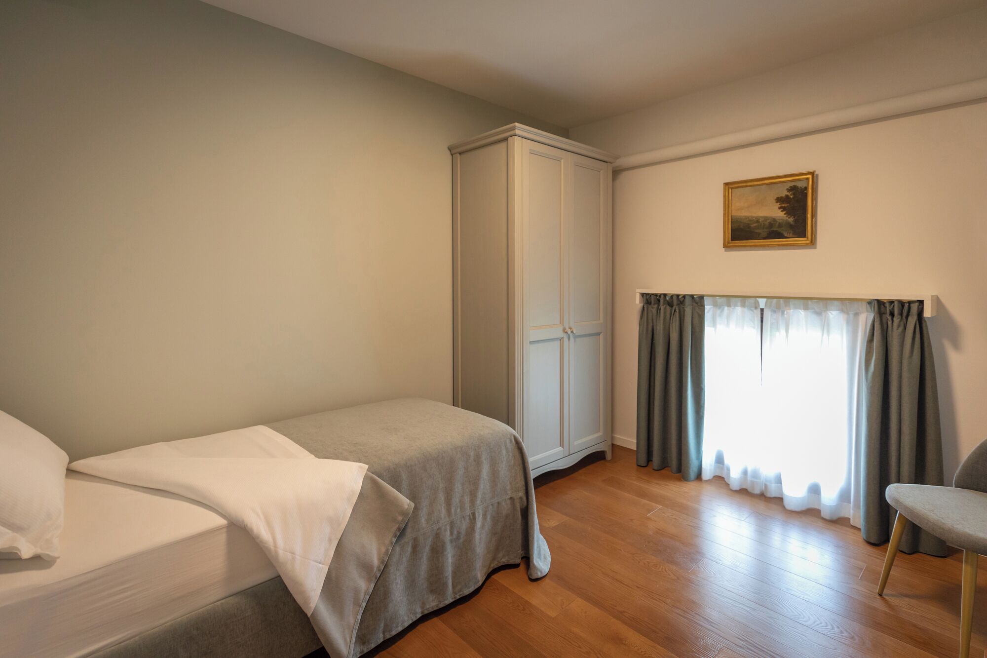 Une chambre à coucher avec un lit, une armoire, une chaise et une fenêtre avec des rideaux.