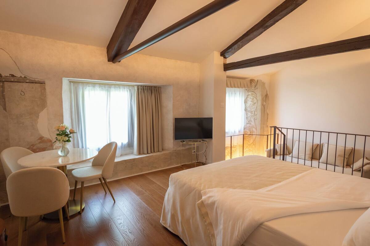 A hotel room with a bed, a desk with a chair, a television, and a window with curtains.