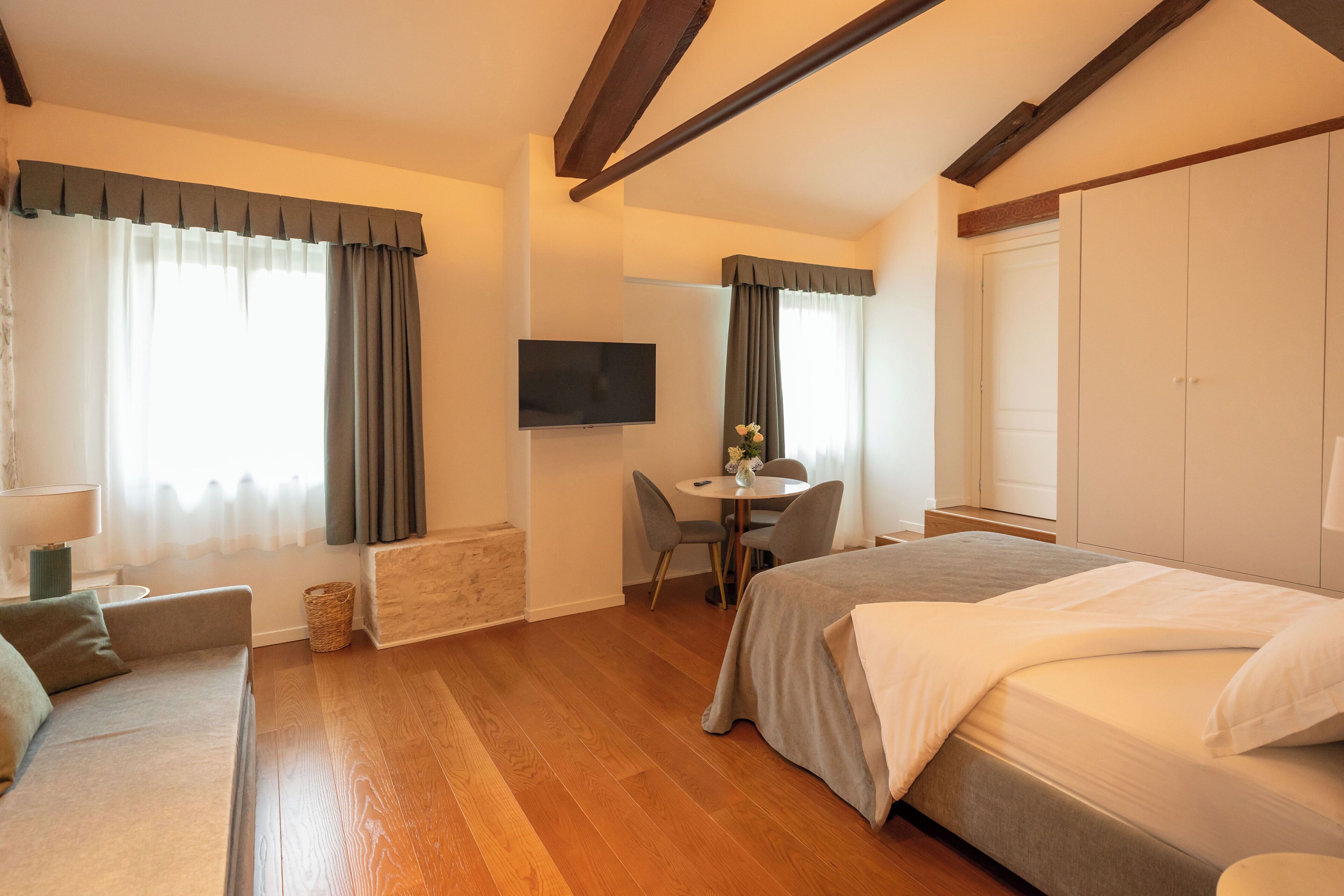 Habitación de hotel con cama, escritorio, silla, televisión y ventana con cortinas.