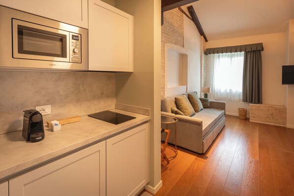 A modern kitchen with a microwave, coffee machine, and a sink. There is a sofa and a small table in the living area. - Castello di Porcìa - Residence (Porcia)