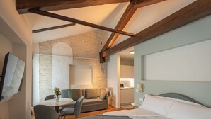 Un dormitorio moderno con una cama grande, un escritorio y una silla. Se ve una zona de cocina al fondo.
